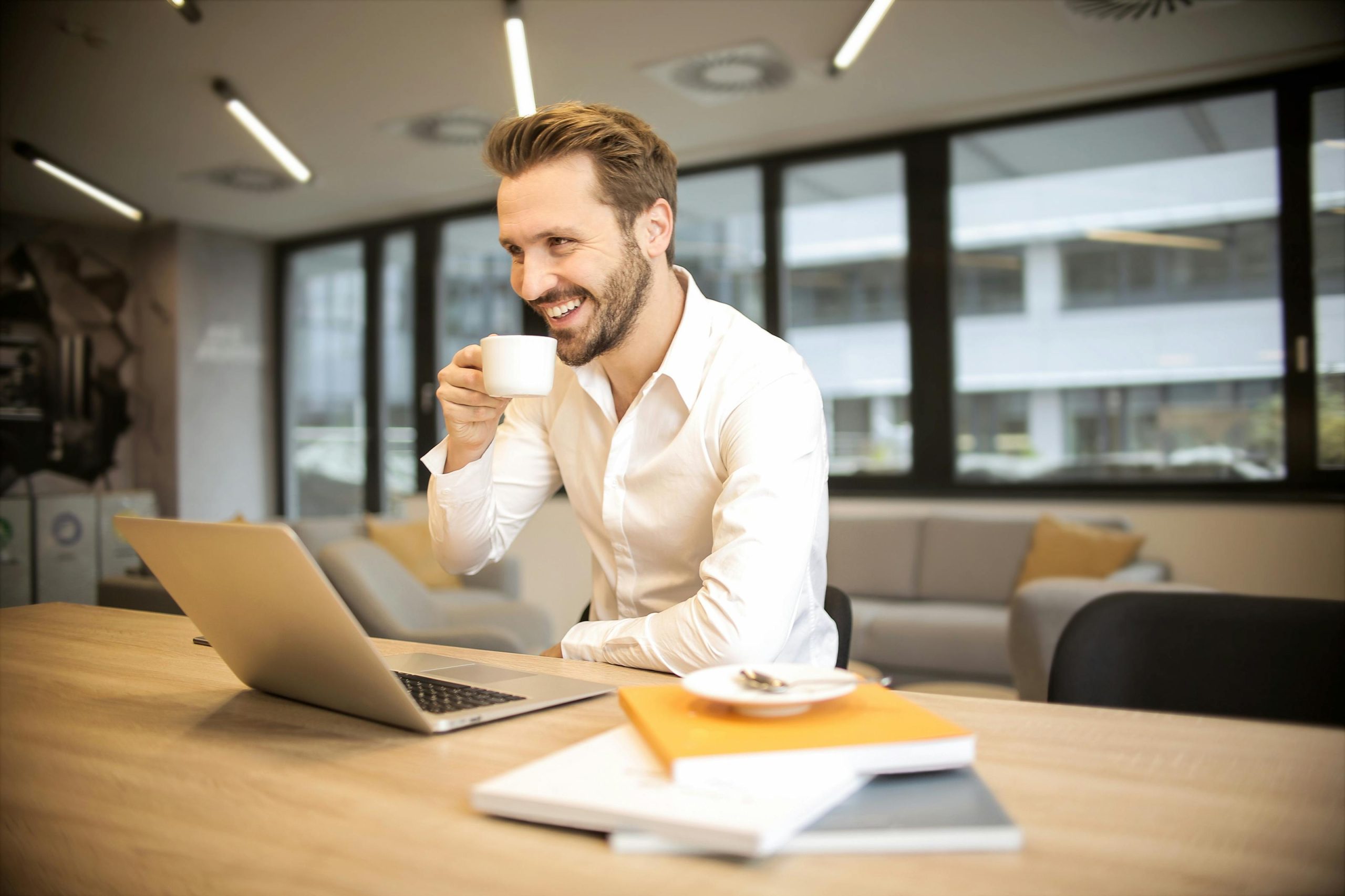 photo of Man Sitting on Chair While Holding Cup in Front of Table